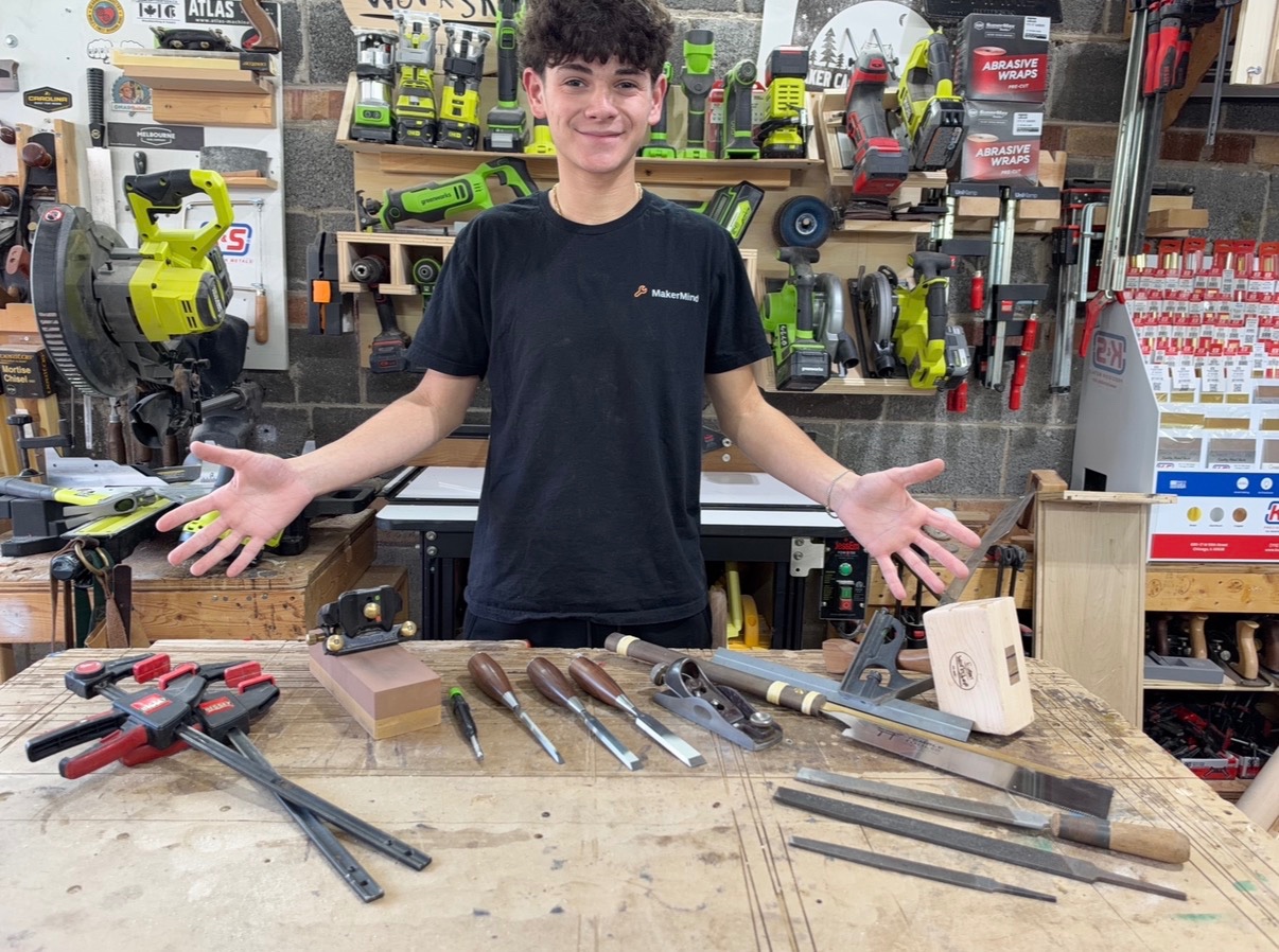 Essential woodworking hand toolsMakerMind founder Evan Sklar standing behind a workbench arranged with essential woodworking hand tools. arranged on a workshop bench