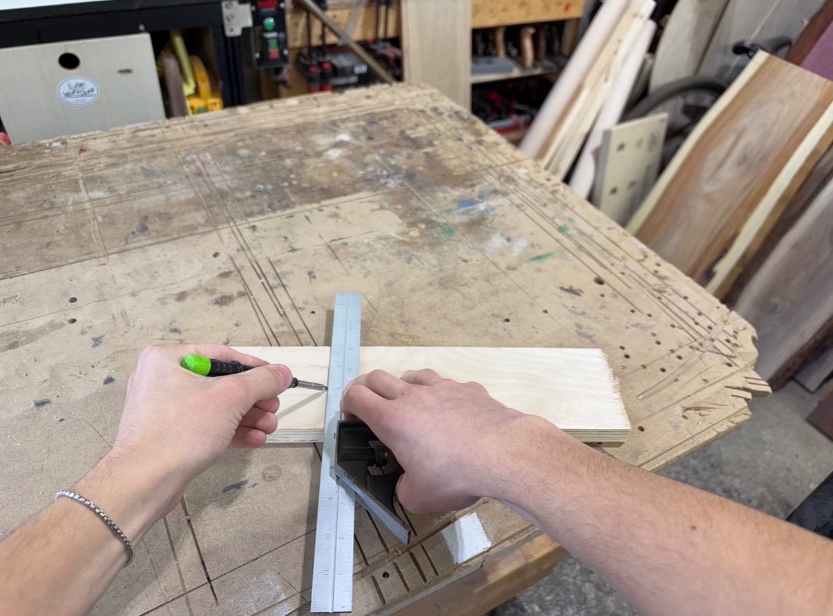 Woodworker using a combination square and pencil to mark a straight line across a wooden board.