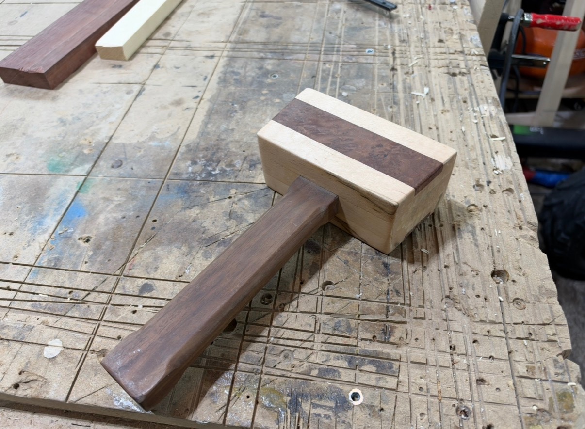 Handmade laminated wooden woodworking mallet resting on a workshop bench.