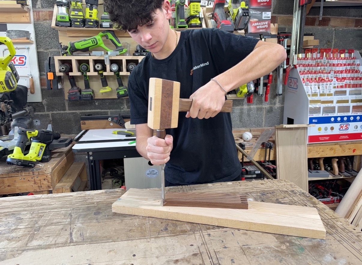 Woodworker using a wooden mallet and chisel to remove material from a secured hardwood board.