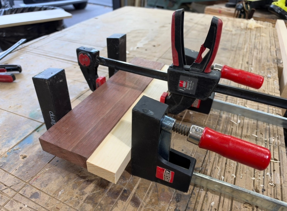 Quick-grip and bar clamps securing hardwood boards flat against a workshop bench.